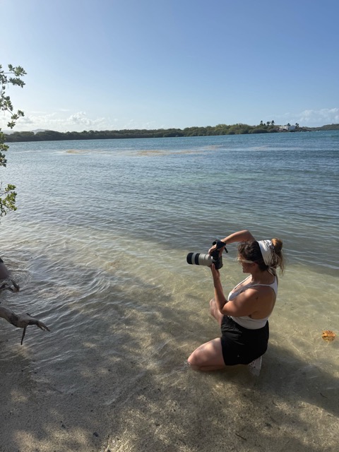 Bri Valiente kneeling in shallow water photographing a destination boudoir session in Puerto Rico
