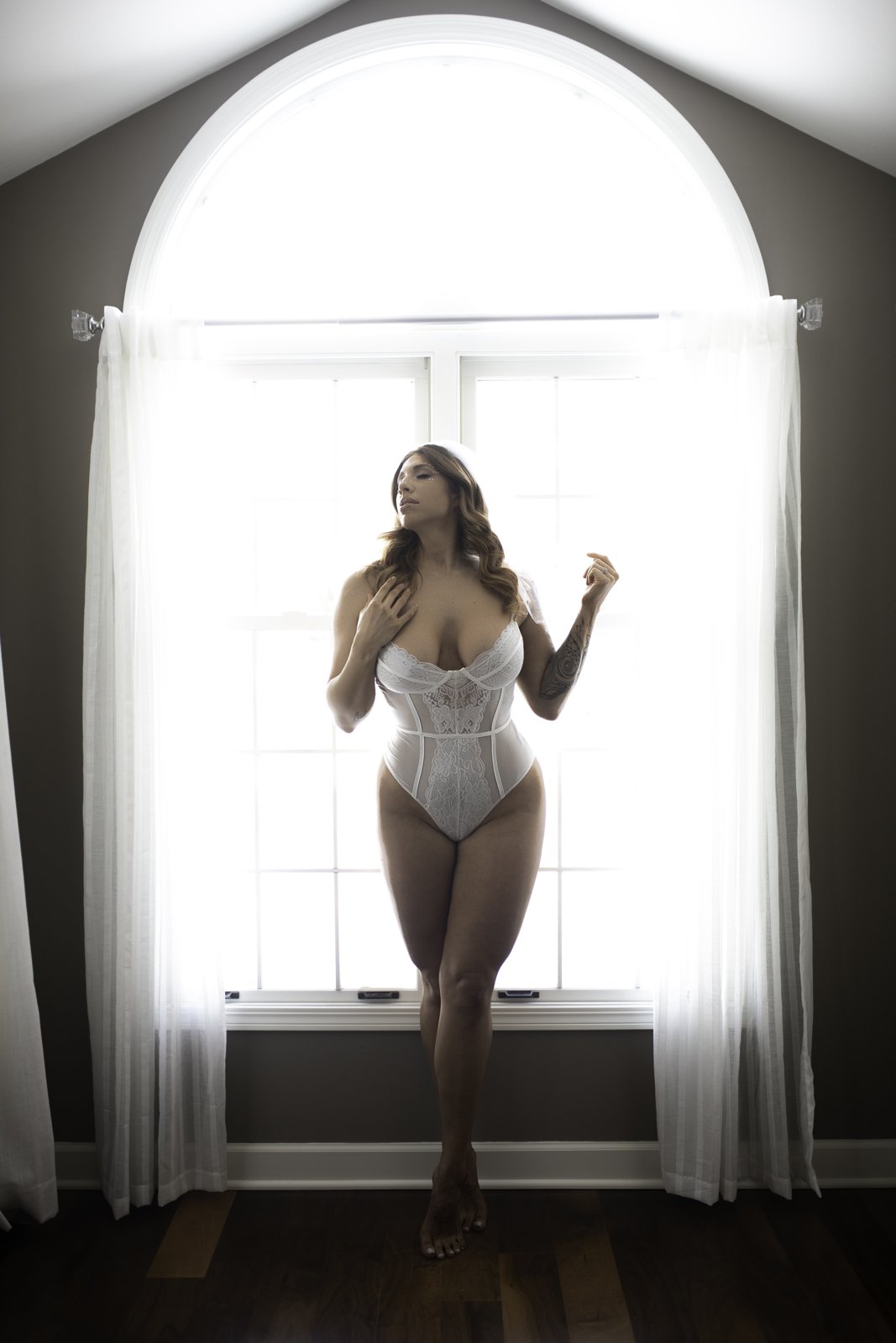 Bride to be in a white lace corset bodysuit in front of an arched window at a Chicago bridal boudoir session